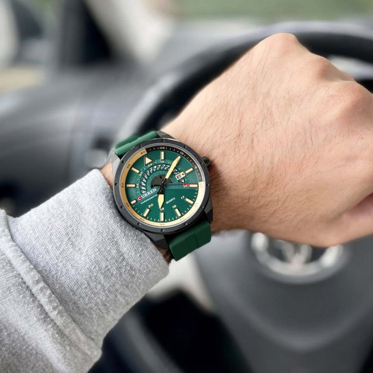 CURREN 8421 green-dial quartz watch worn on the wrist at a car steering wheel