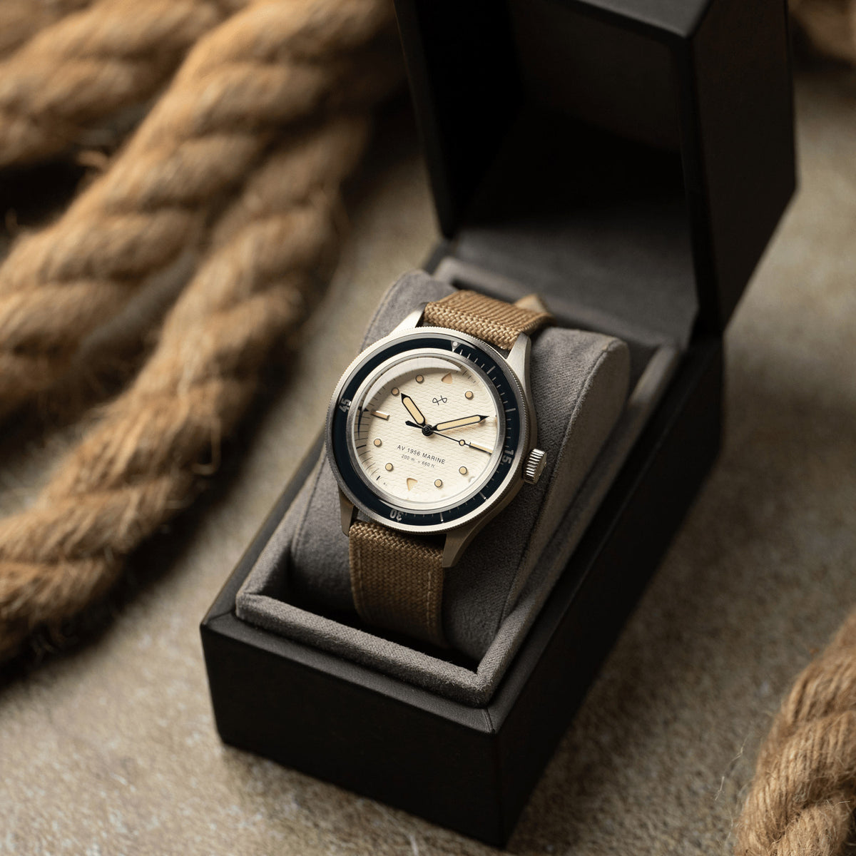 AV86 1956 Marine automatic watch with off-white dial and navy bezel on a beige strap, resting in its presentation box beside a coiled rope