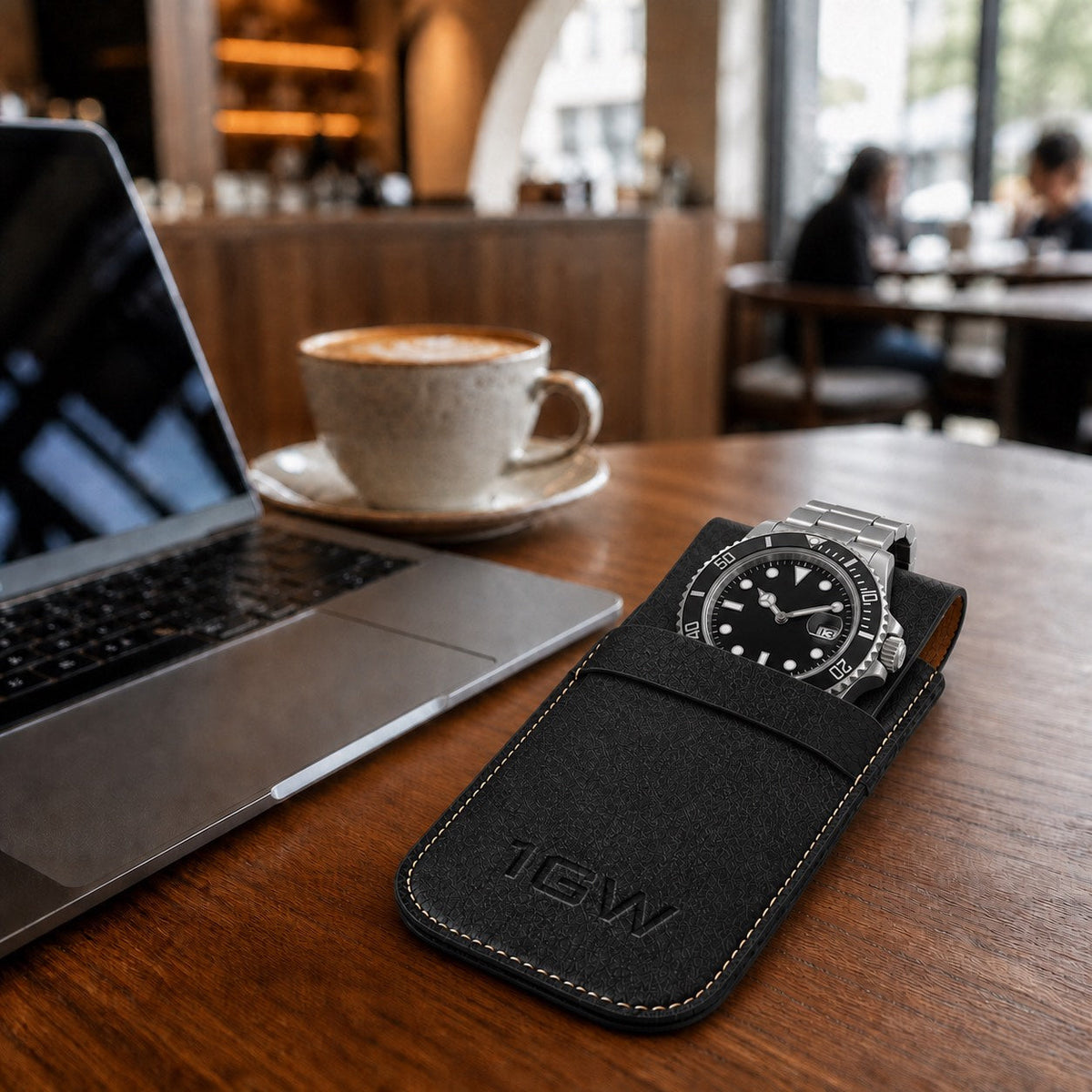 Black 1GW watch travel pouch with premium diver-style watch beside a laptop in a coffee shop