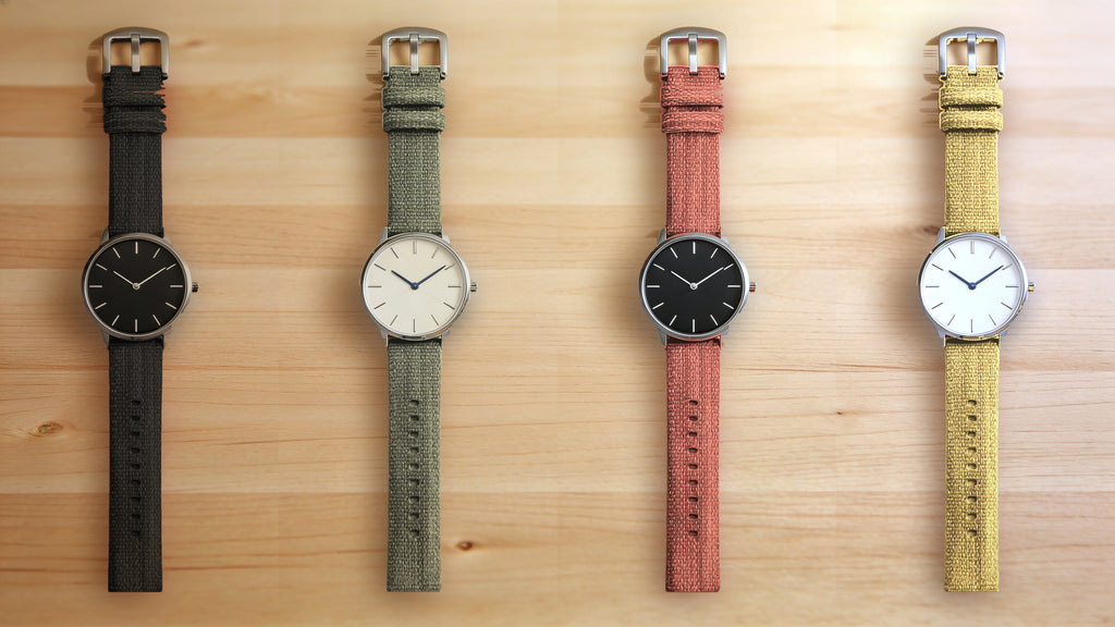1GW Black, Green, Orange and Yellow braided canvas watch straps, top-down flat lay on a light maple wood table