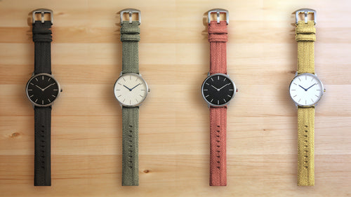 1GW Black, Green, Orange and Yellow braided canvas watch straps, top-down flat lay on a light maple wood table