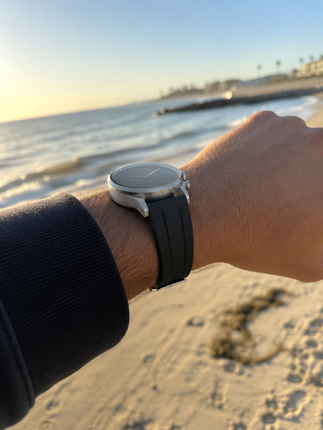 Customer-style iPhone wrist photo with black silicone strap at beach