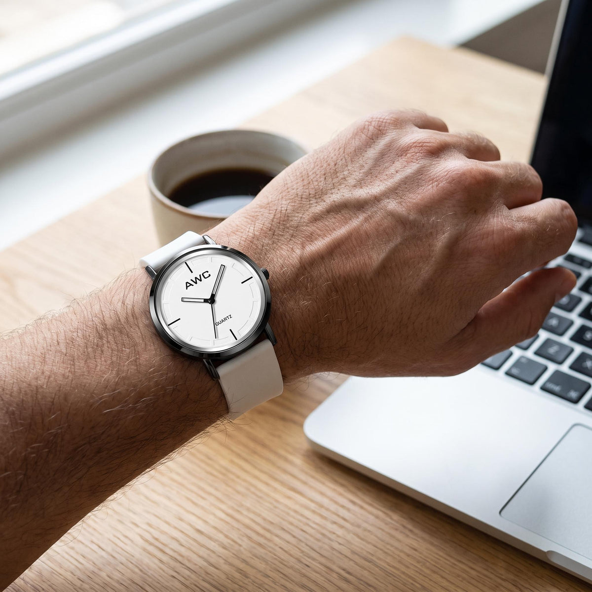 AWC Minimalist Quartz white dial watch worn on the wrist at a desk beside a laptop and coffee