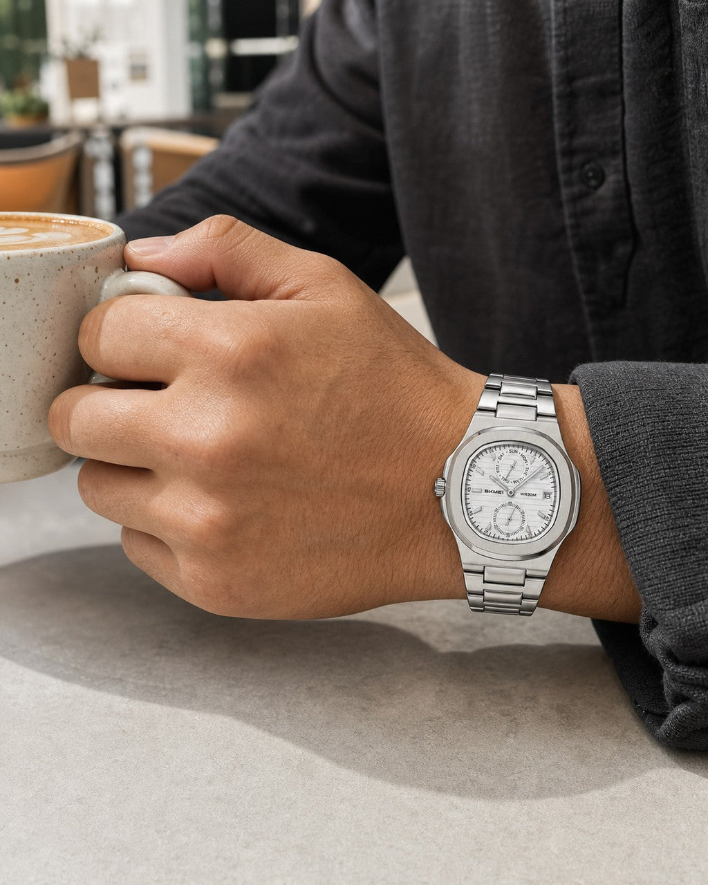 SKMEI 2423 silver case white dial watch worn on the right wrist while holding a coffee cup
