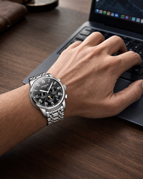 Carnival moonphase automatic watch with black dial and stainless steel bracelet worn while using a laptop