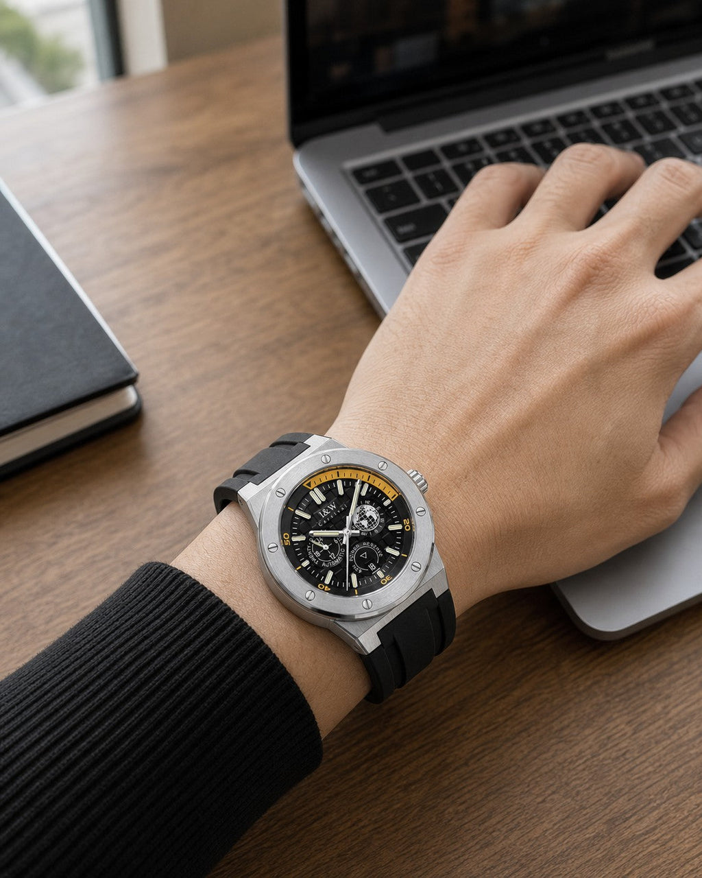 I&W Carnival IW783G black and gold automatic watch worn correctly on the outside of the wrist while working at a laptop