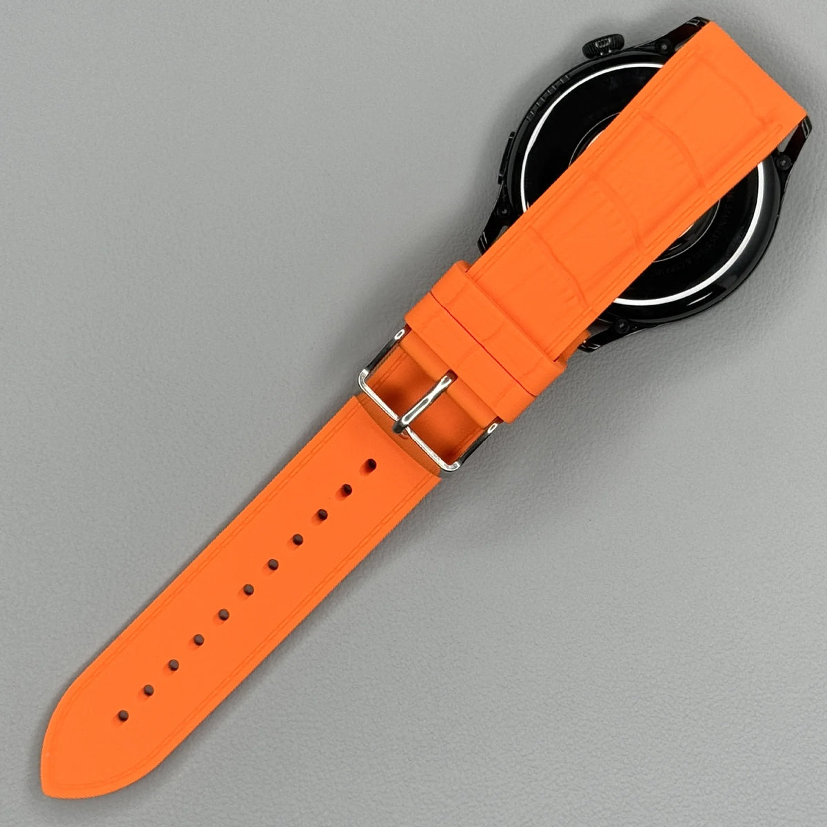 1GW Orange leather-texture silicone watch strap curled beside a watch, showing the embossed grain