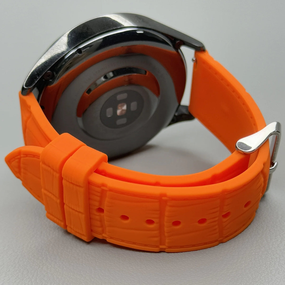 Close-up of the 1GW Orange leather-texture silicone strap fitted to a watch caseback with quick-release bars