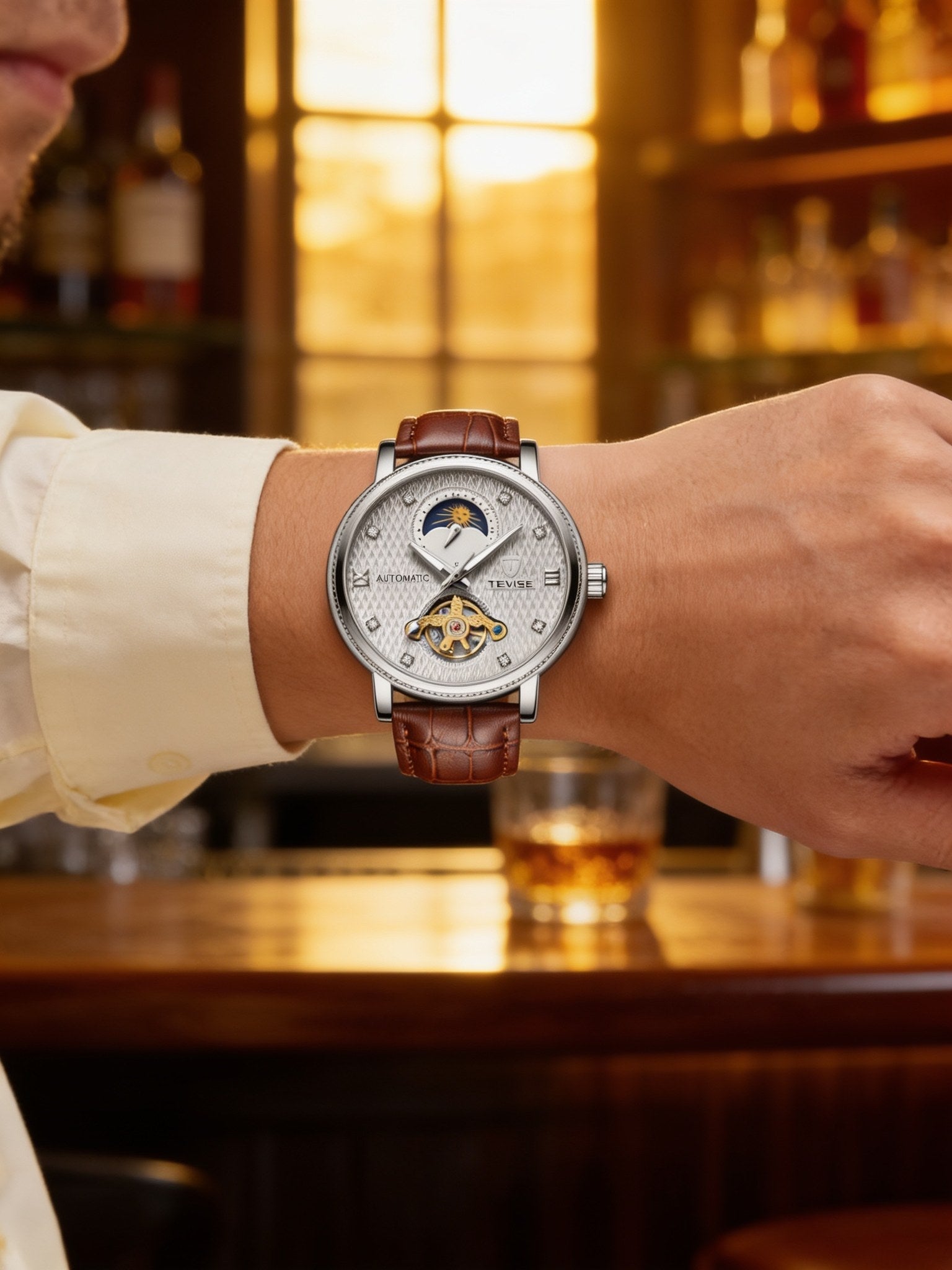 TEVISE silver-white open-heart automatic dress watch with brown leather strap, worn on wrist at a bar in warm light