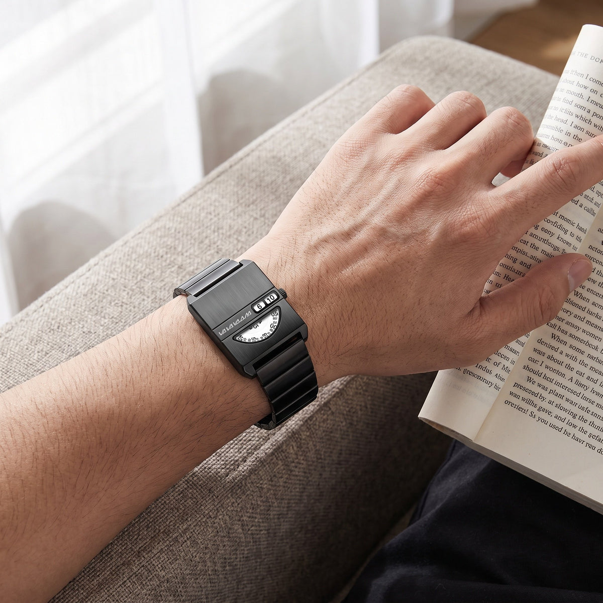 VA VA VOOM No-Hands Square watch in black worn on the wrist while reading a book on a couch