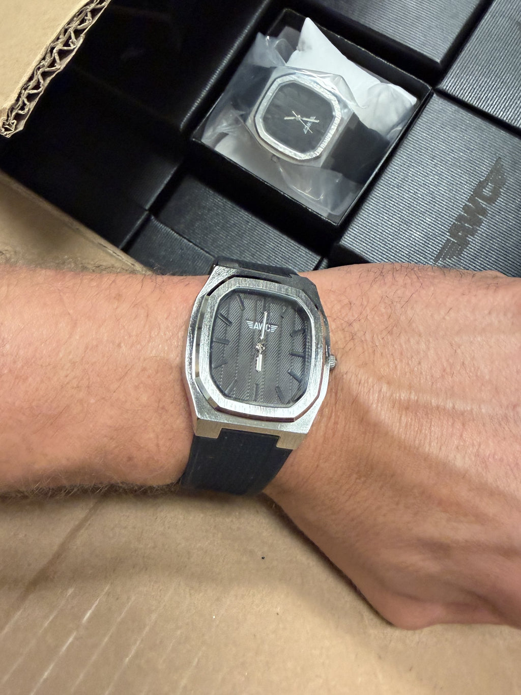 AWC square quartz watch in black worn on the wrist next to AWC gift boxes