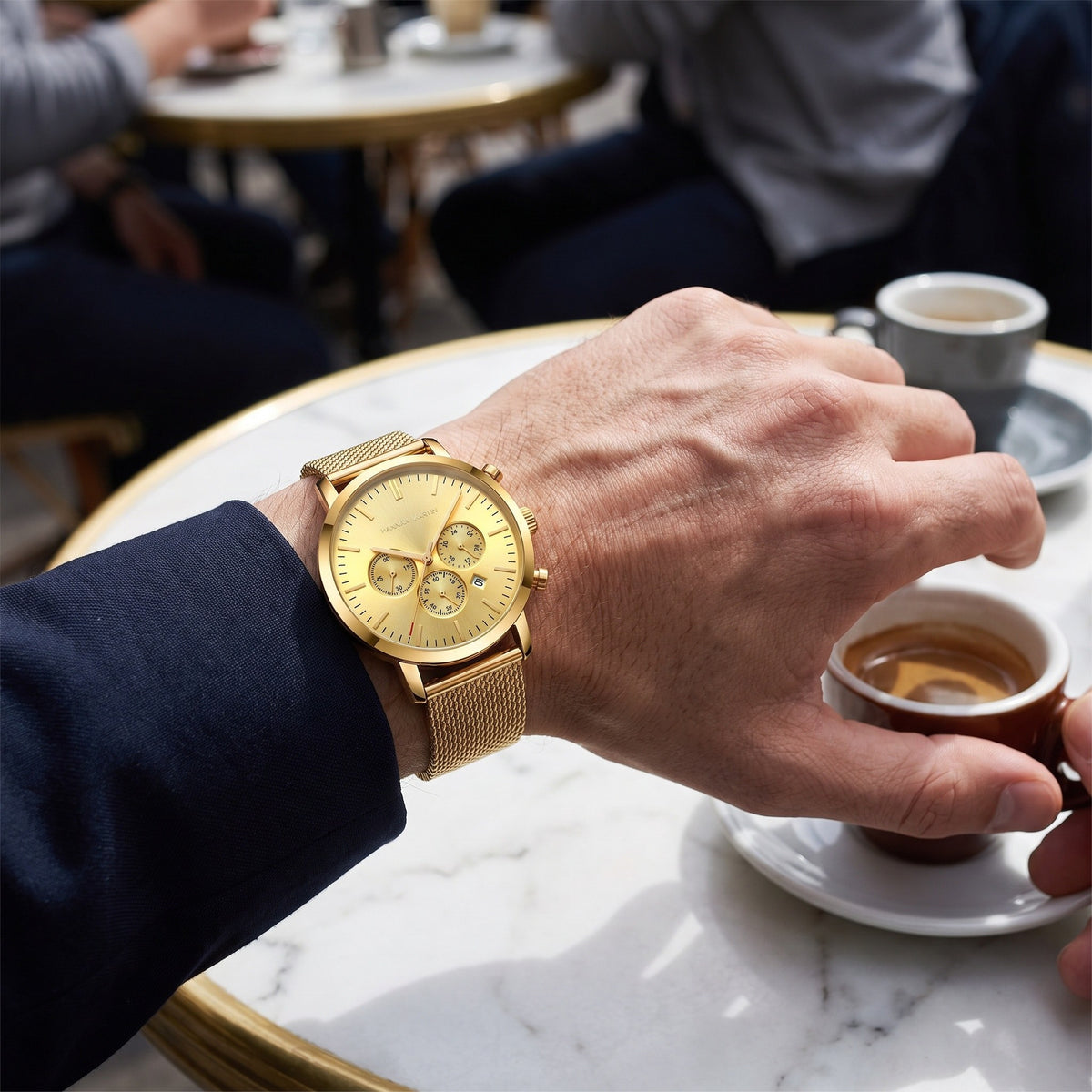 HANNAH MARTIN Three-Subdial Mesh 45mm in gold worn on the wrist at a cafe table with an espresso