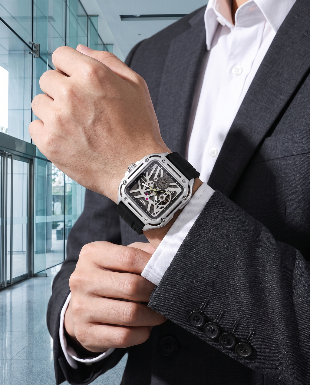 Man in charcoal suit wearing FIDI silver square skeleton automatic watch