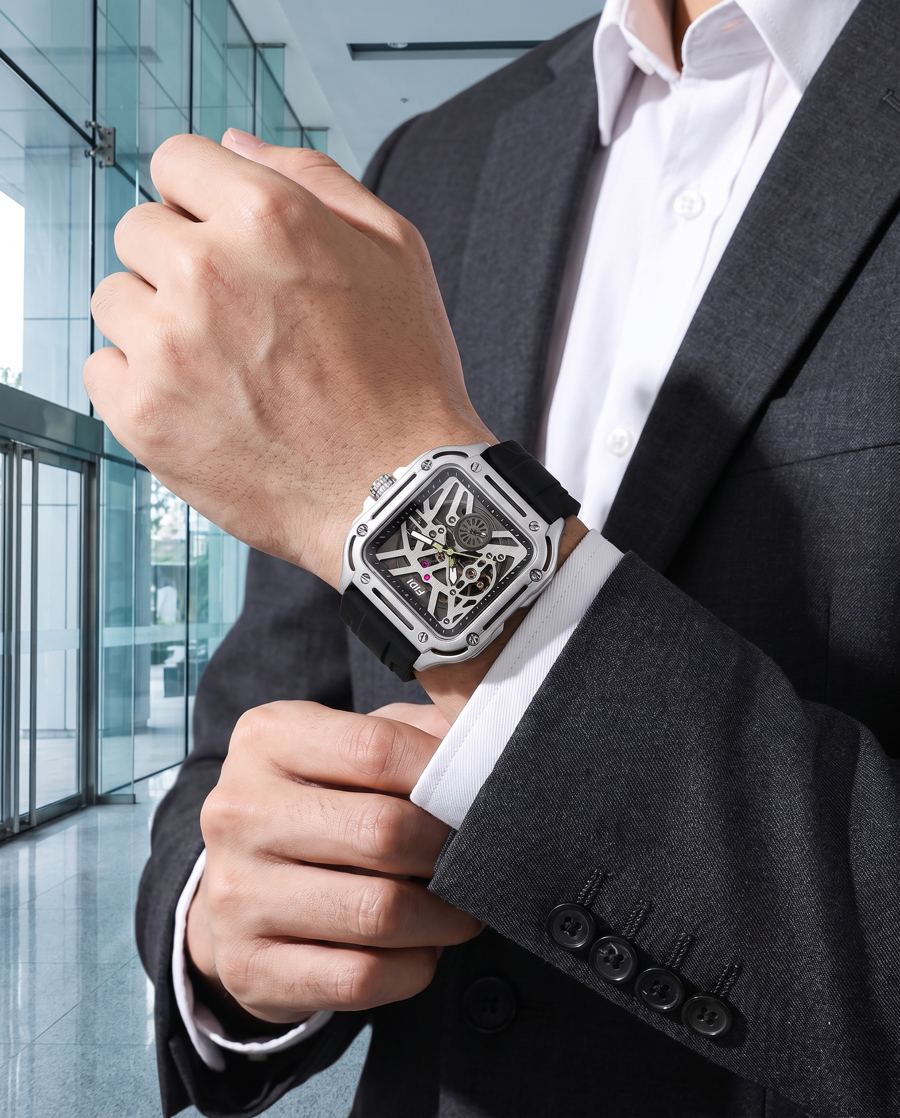 Man in charcoal suit wearing FIDI silver square skeleton automatic watch