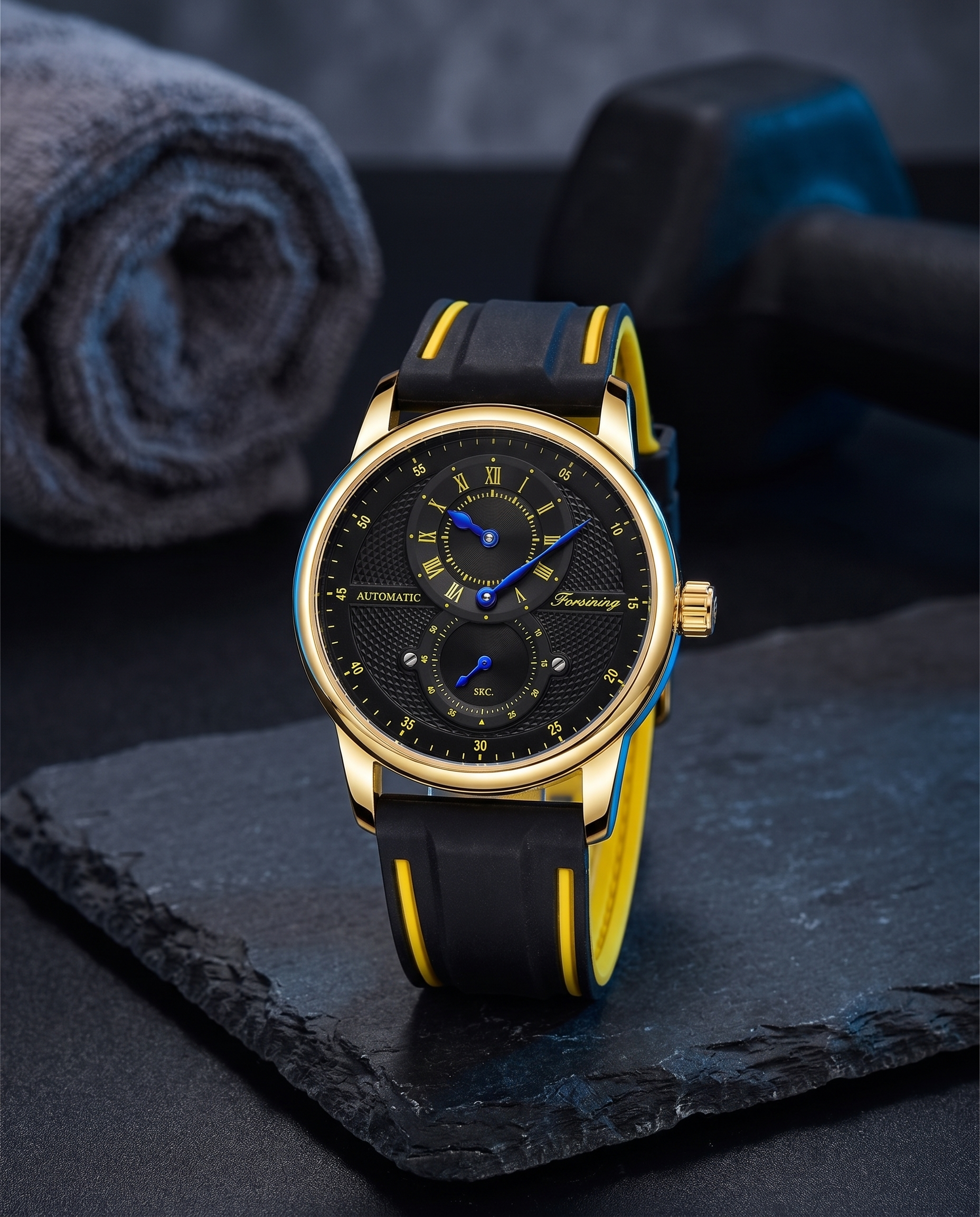 FORSINING 43mm automatic sport watch in Gold / Black beside a gym towel and dumbbell