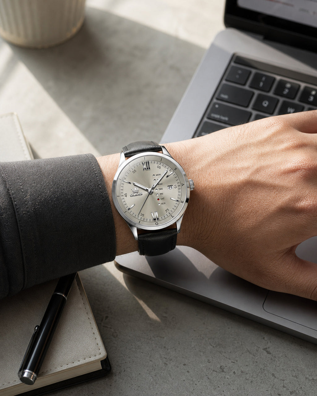 OLEVS Gray day-date watch worn at a laptop