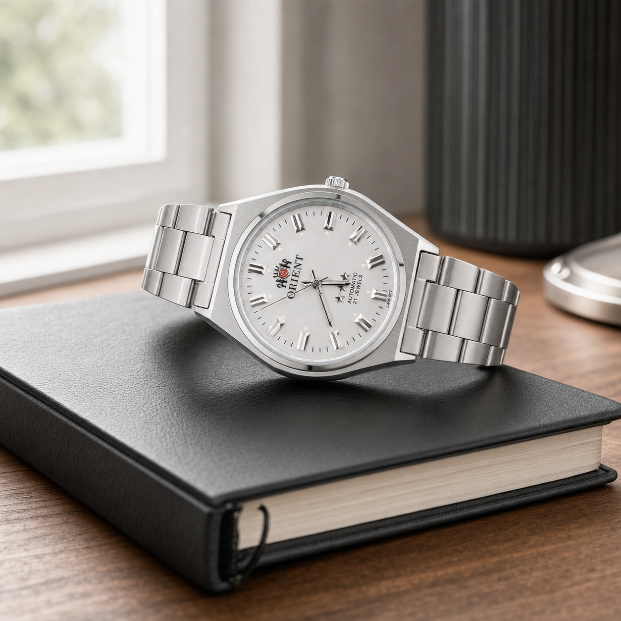 Orient 3 Stars L469-D12 silver automatic watch on a charcoal leather notebook in natural office light