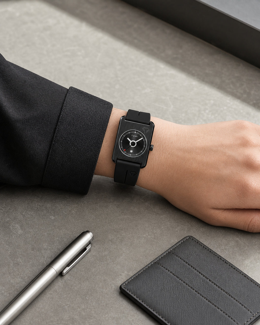 TOMI all-black TV-dial watch worn at a stone desk